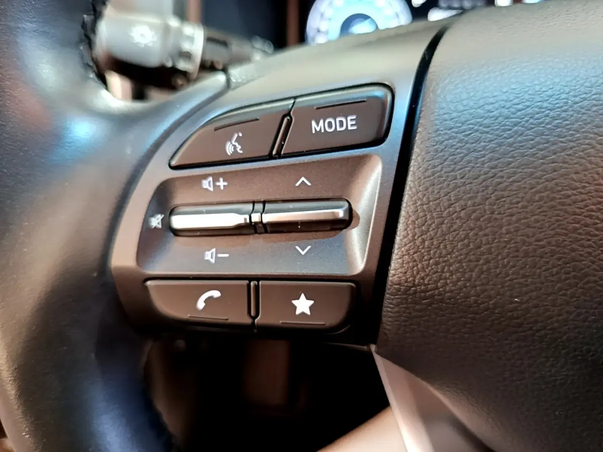 Gros plan sur les commandes du volant cuir multifonctions du Hyundai Kona électrique, boutons de volume et mode visibles.