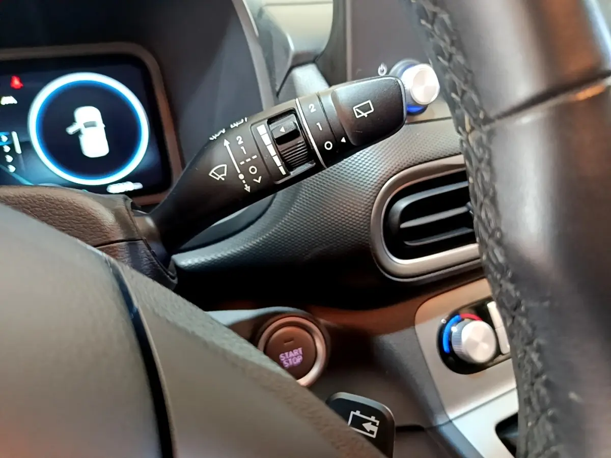 Vue intérieure rapprochée du volant cuir et des commandes de la Hyundai Kona électrique, avec tableau de bord et bouton start/stop visibles.