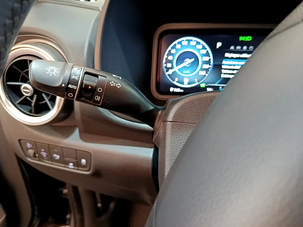 Gros plan sur le commodo gauche et le tableau de bord numérique bleu du Hyundai Kona électrique, intérieur noir.