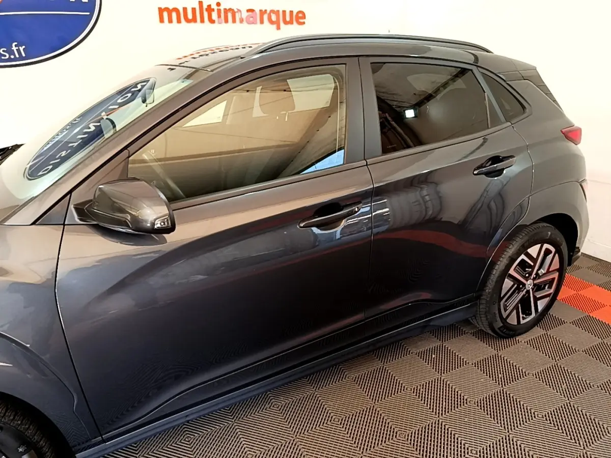 Vue latérale côté gauche d'une Hyundai Kona électrique 2021 gris foncé avec jantes spécifiques et rétroviseurs assortis.