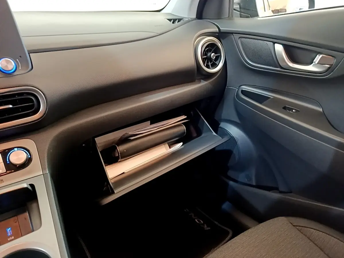 Vue intérieure côté passager du tableau de bord noir d'une Hyundai Kona électrique avec boîte à gants ouverte contenant des documents.