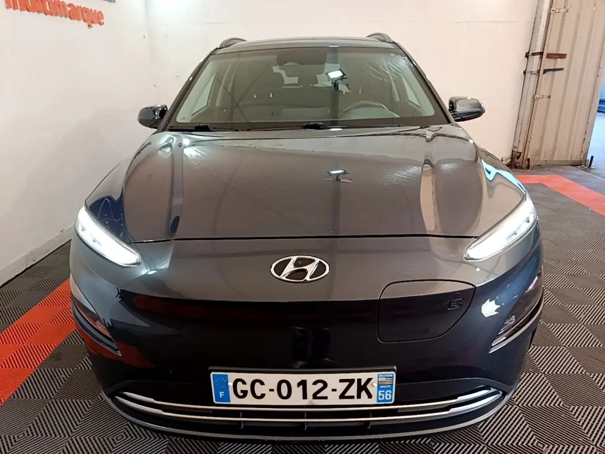 Vue de face d'un Hyundai Kona électrique gris foncé avec phares LED allumés dans un garage.