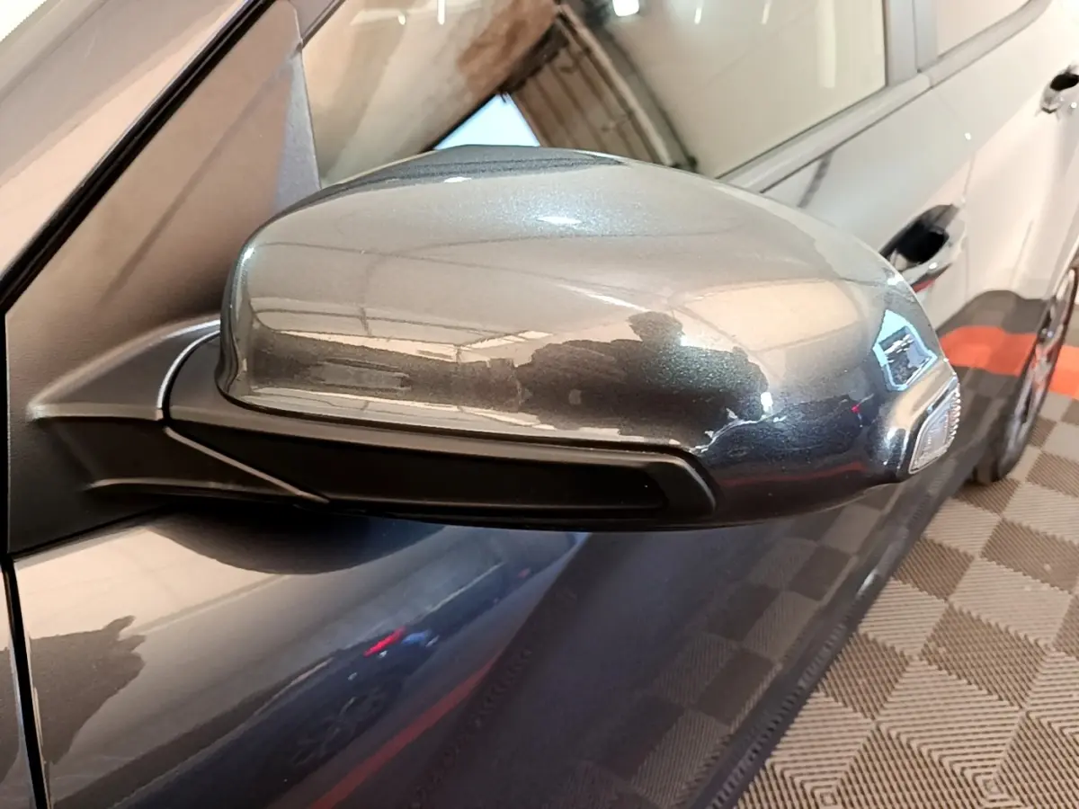 Rétroviseur côté conducteur gris métallisé d'une Hyundai Kona électrique 2021, avec carrosserie sombre visible en arrière-plan.