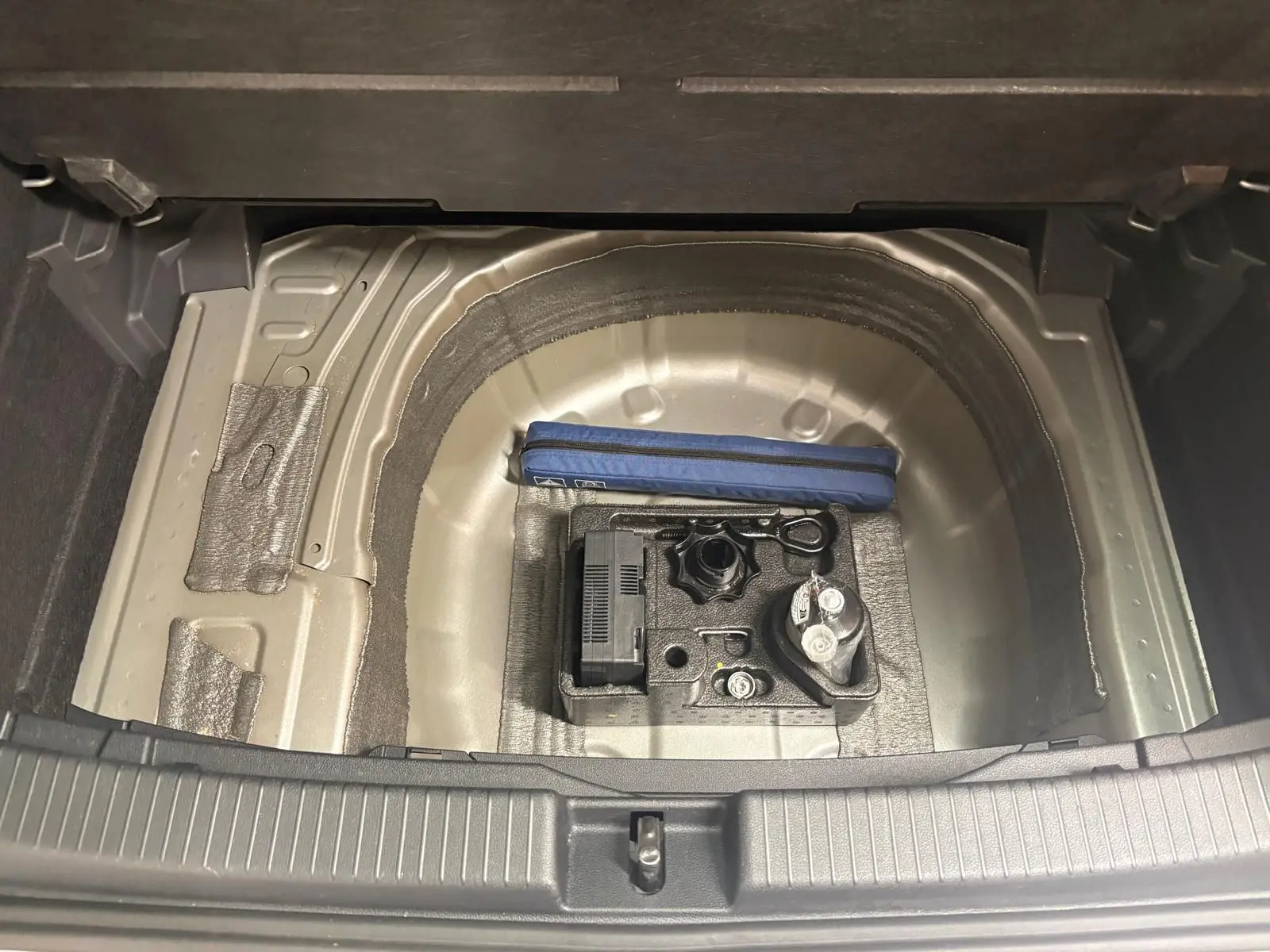 Coffre ouvert du Volkswagen T-Cross 2024, vue sur le compartiment à roue de secours avec kit de dépannage visible.