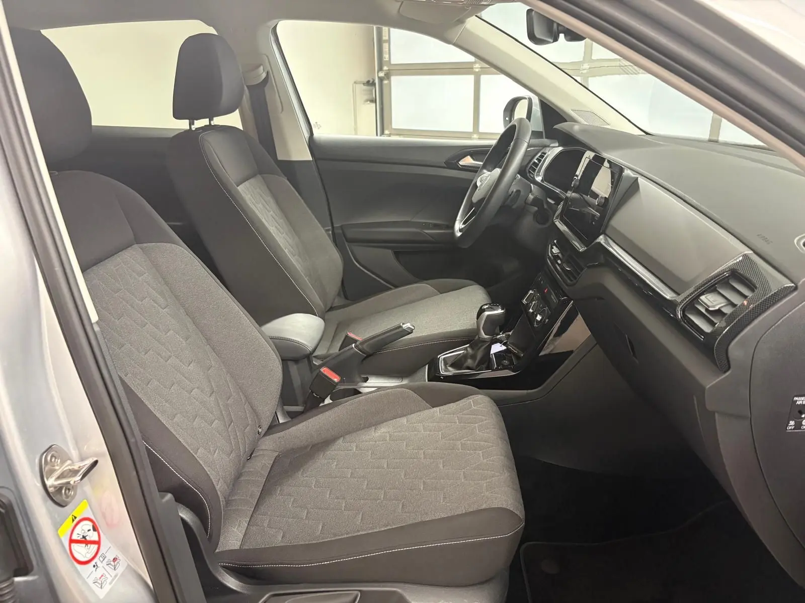 Intérieur avant du Volkswagen T-Cross 2024 en reflet d'argent, montrant sièges tissu gris et tableau de bord noir.