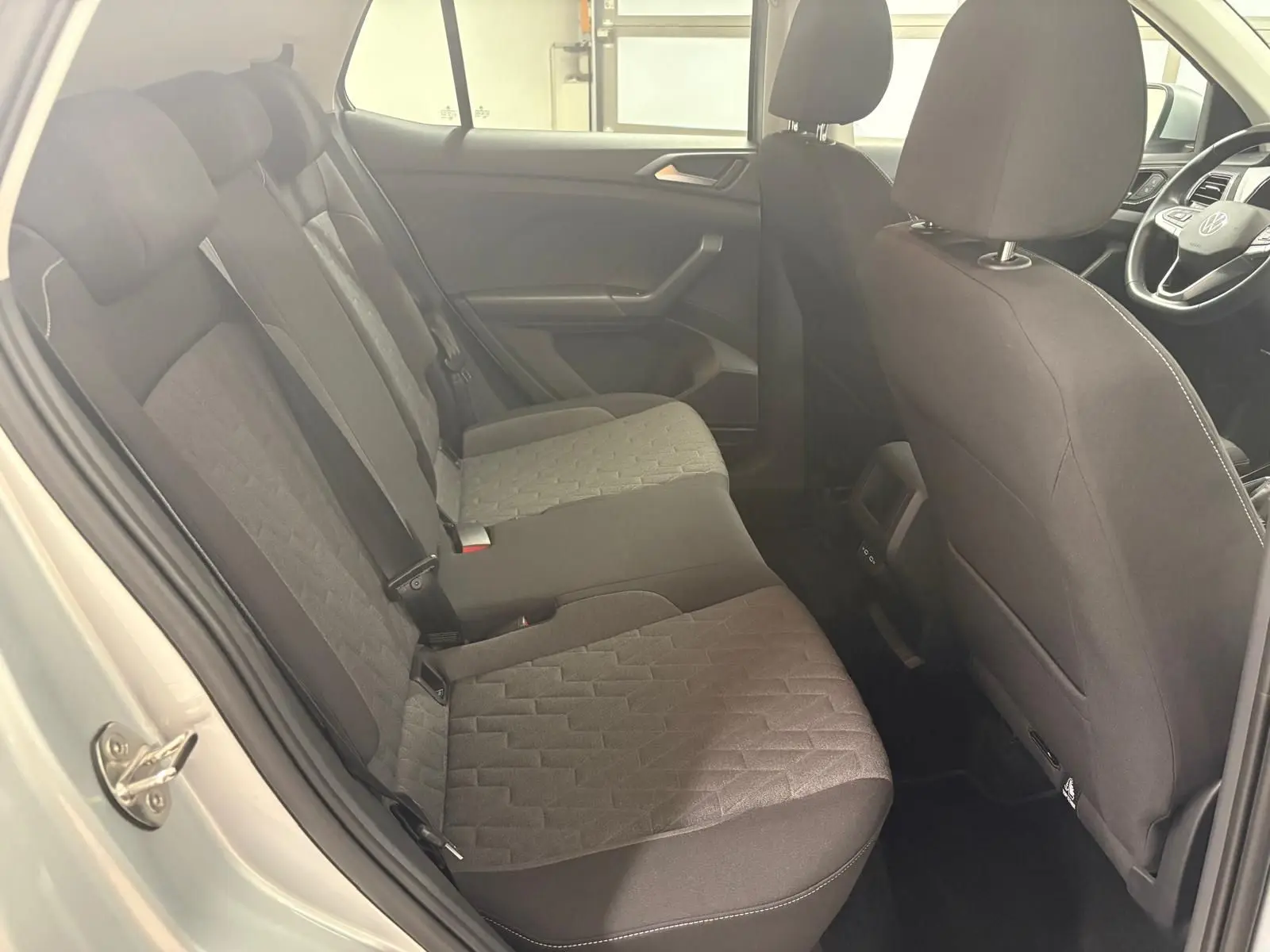 Vue intérieure côté gauche sur la banquette arrière et sièges avant noirs du Volkswagen T-Cross reflet d'argent 2024.
