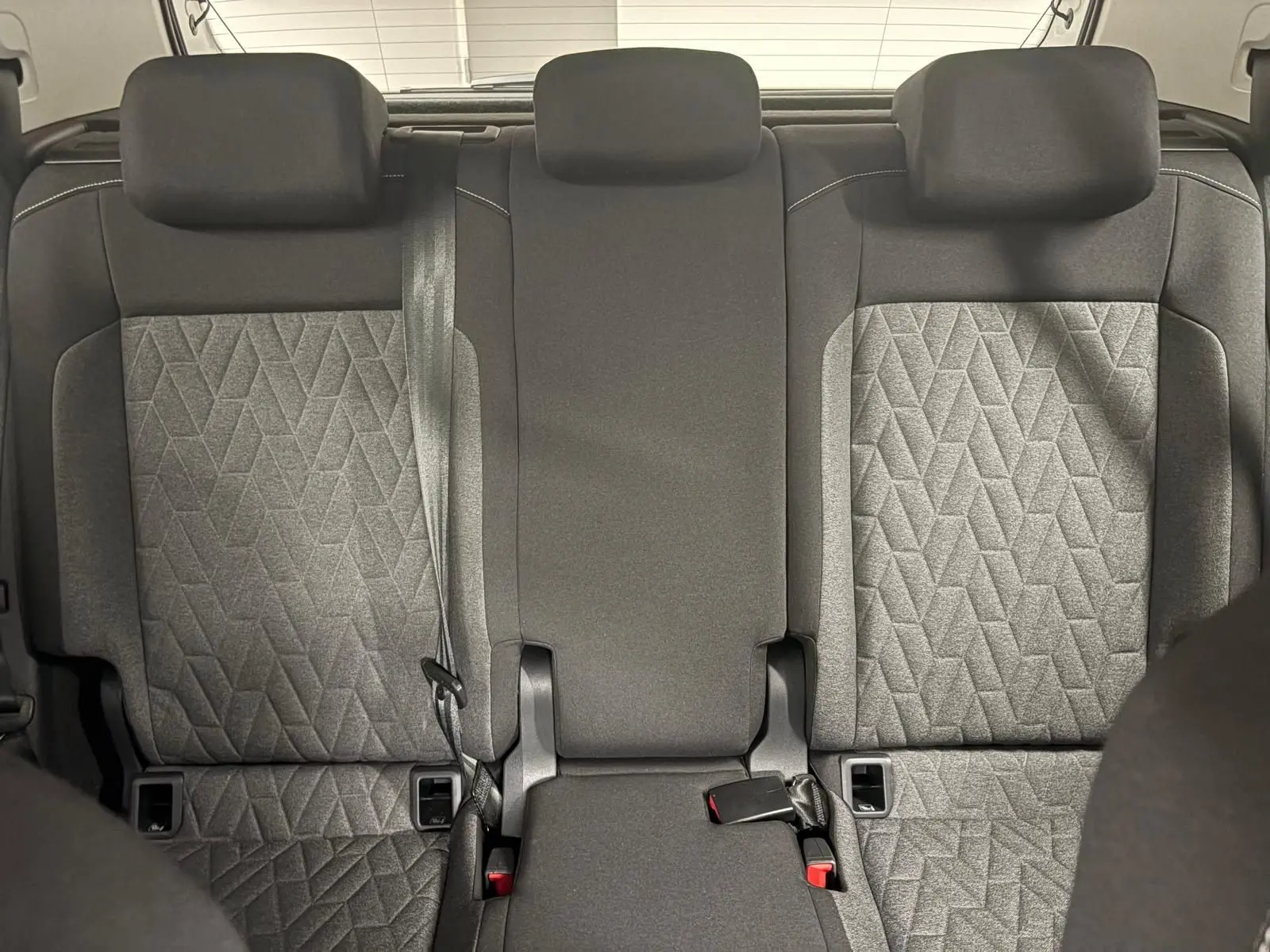 Vue intérieure arrière du Volkswagen T-Cross 2024, sièges tissu gris avec motifs géométriques et appuis-tête intégrés.