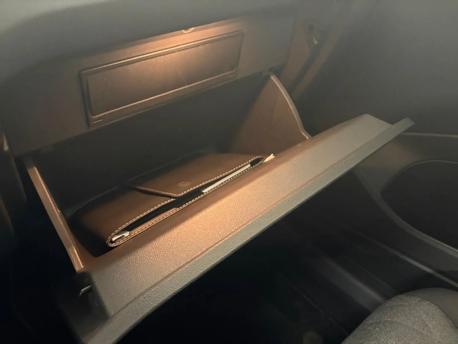 Gant de boîte à gants ouvert côté passager avec un étui noir à l'intérieur, intérieur sombre du Volkswagen T-Cross.