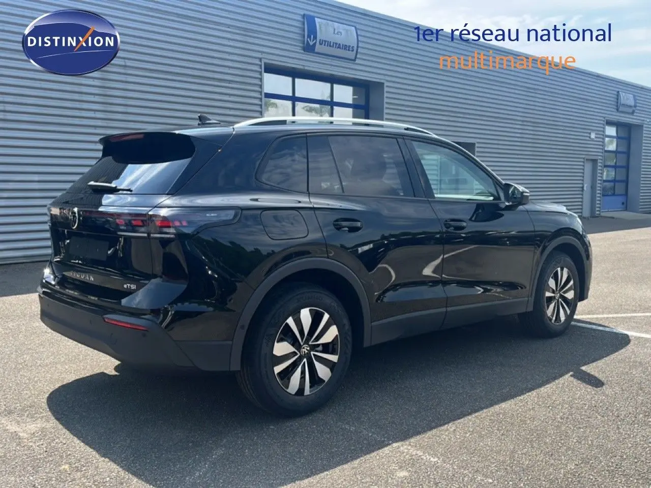 Vue 3/4 arrière droite d'un Volkswagen Tiguan noir Grenadilla métallisé stationné devant un bâtiment industriel.