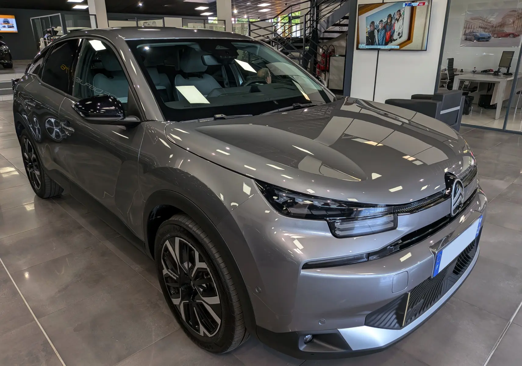 Citroën C4 hybride gris Mercury vue 3/4 avant droit en intérieur, avec jantes biton et calandre distinctive.