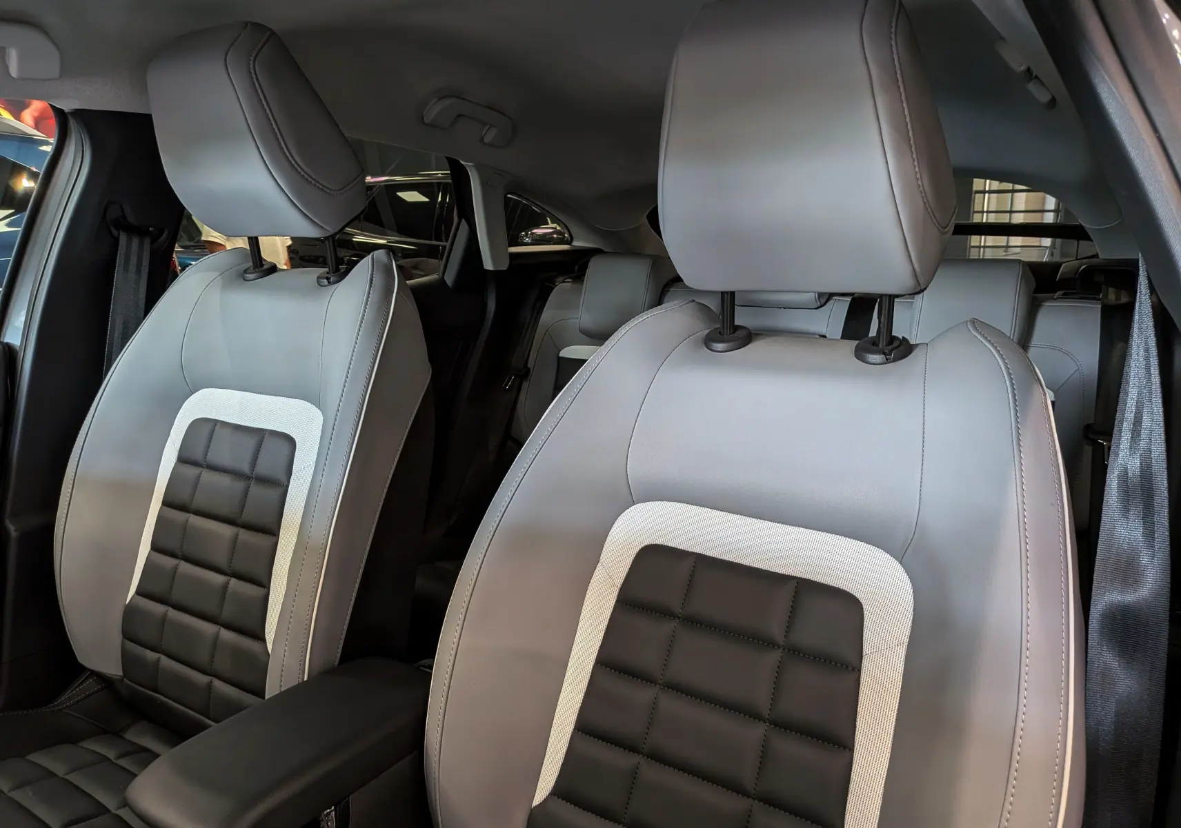 Vue rapprochée des sièges avant en cuir noir et gris clair de la Citroën C4 Hybride 2025, intérieur élégant.