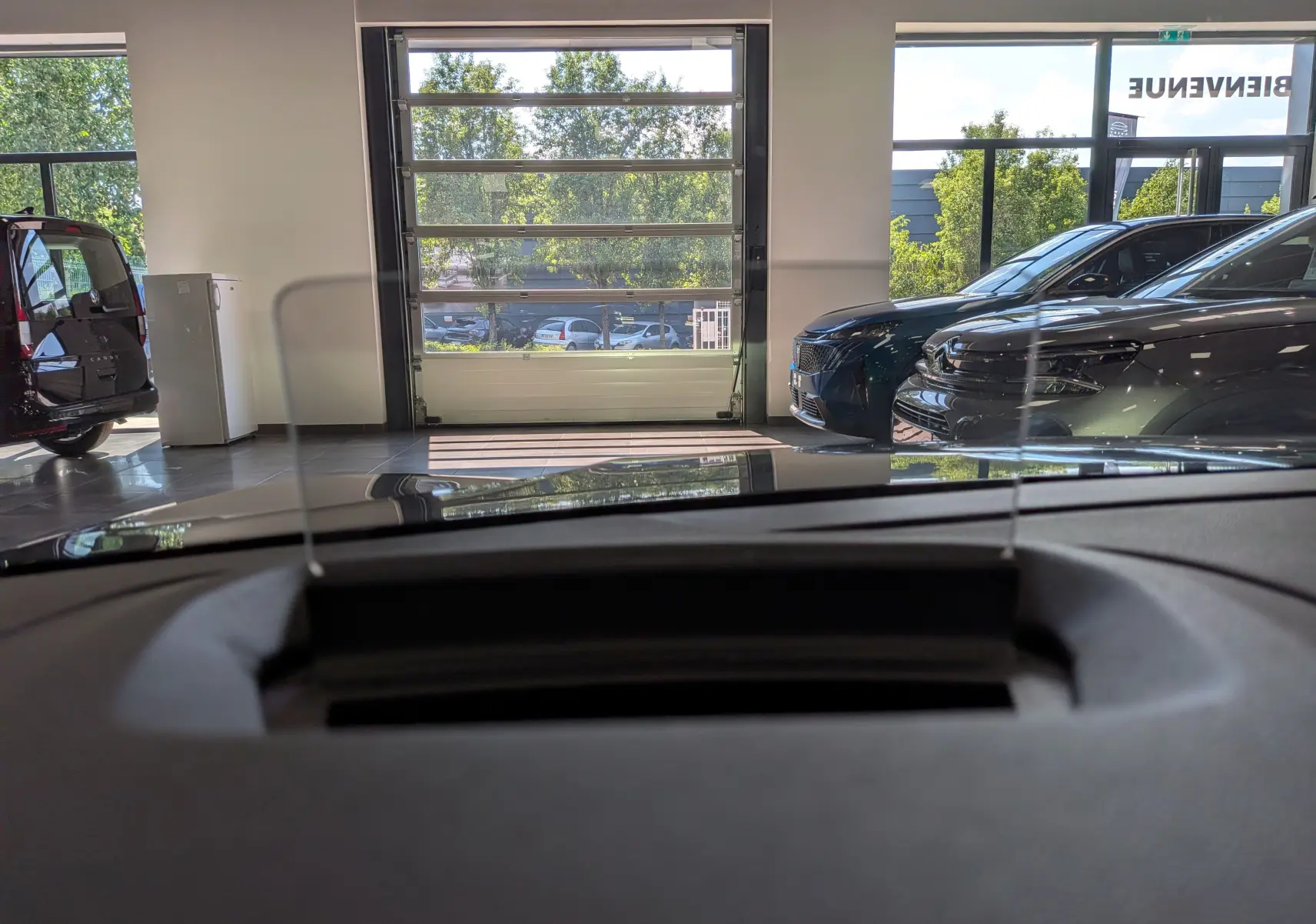 Vue intérieure du tableau de bord de la Citroën C4 Hybride 2025, avec affichage tête haute et vue sur le showroom.