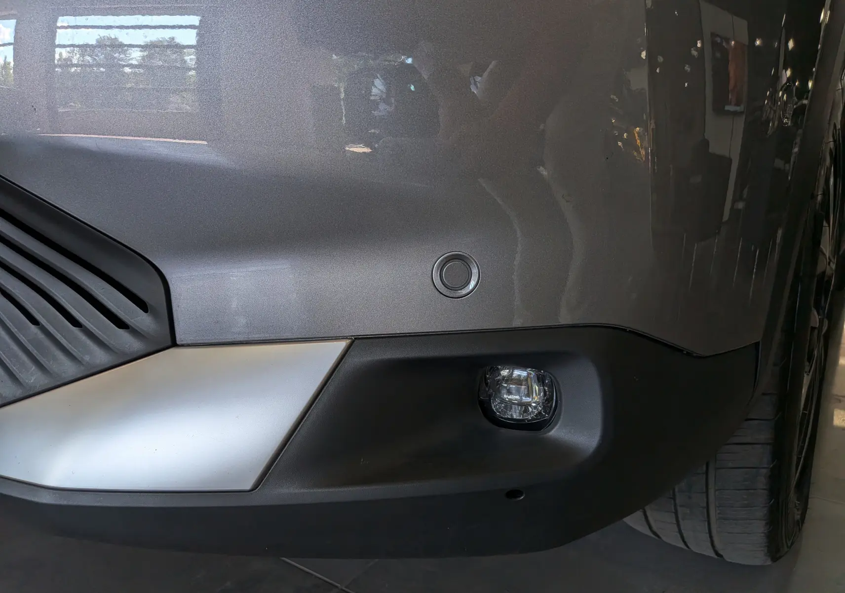 Gros plan sur le pare-chocs avant gris Mercury du Citroën C4 hybride 2025 avec feu antibrouillard et capteur de stationnement.