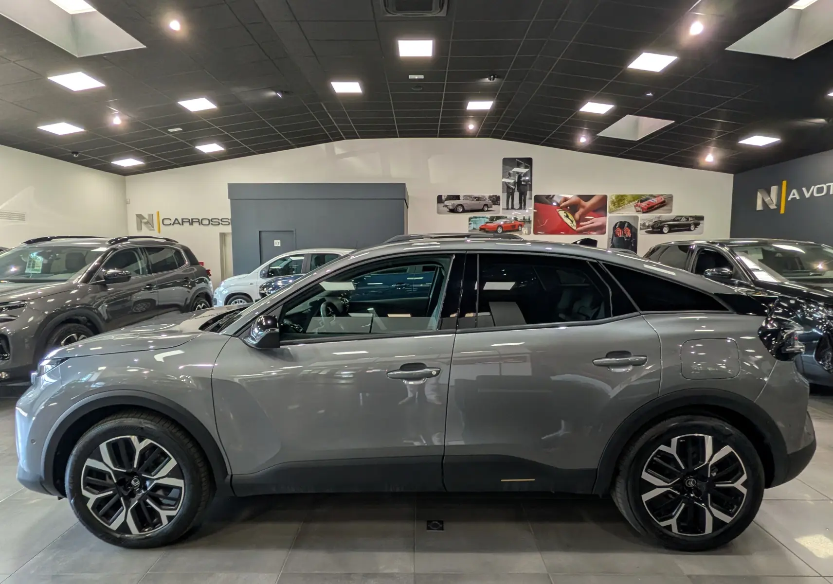 Profil latéral droit d'une Citroën C4 Hybride 145 CH e-DCS6 MAX gris Mercury en showroom, avec jantes biton noires et toit noir.