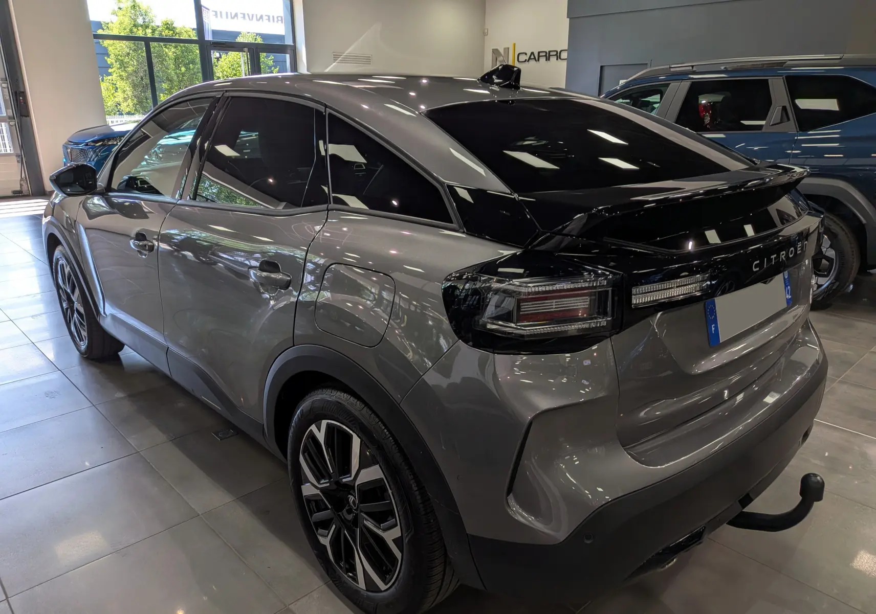 Vue 3/4 arrière droite d'une Citroën C4 hybride gris Mercury avec toit noir et attelage visible en showroom.