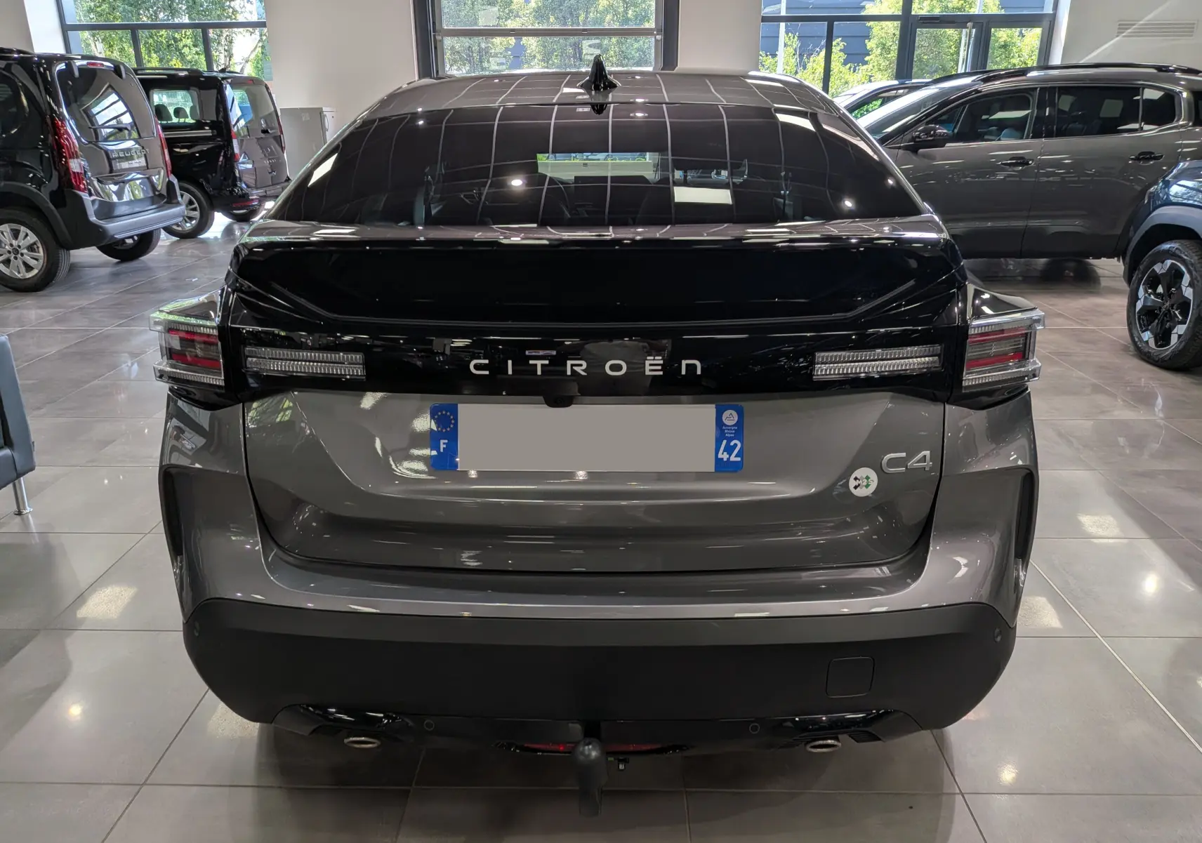 Vue arrière d'une Citroën C4 hybride gris Mercury avec toit noir brillant et feux arrière étirés en intérieur showroom.