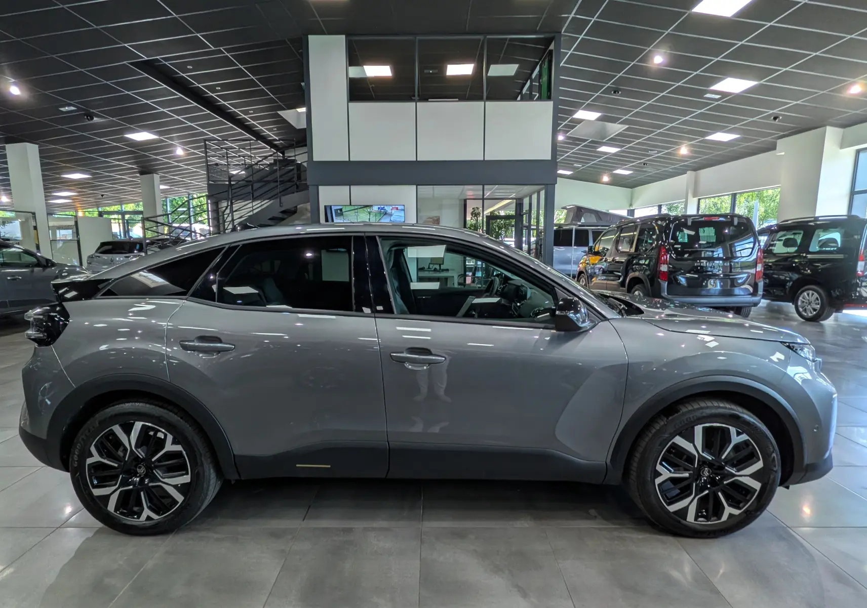 Vue de profil côté gauche d'une Citroën C4 hybride gris Mercury en intérieur, avec jantes noires et toit noir contrastant.