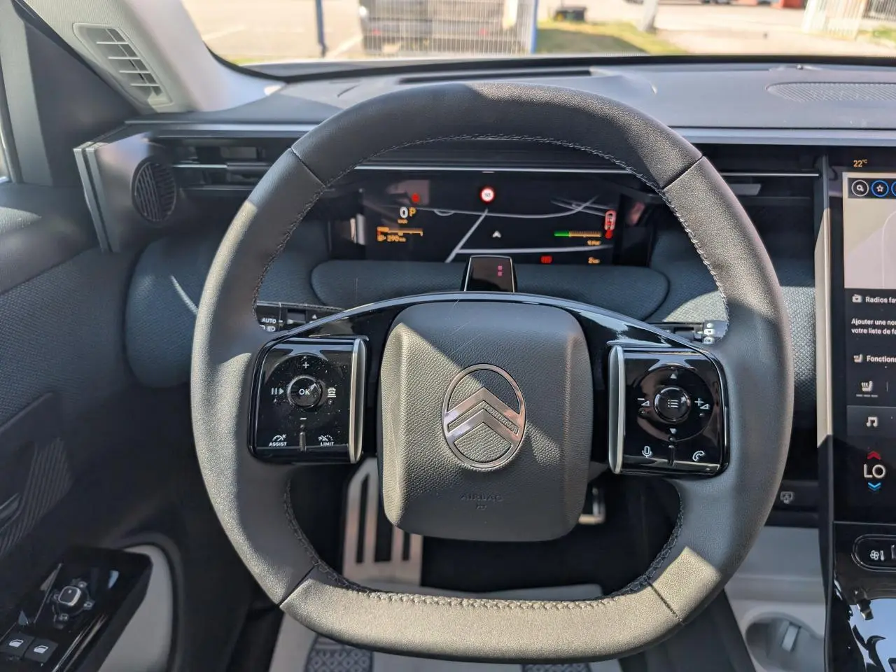 Vue rapprochée du volant noir mat au logo Citroën, avec tableau de bord numérique et écran tactile latéral.