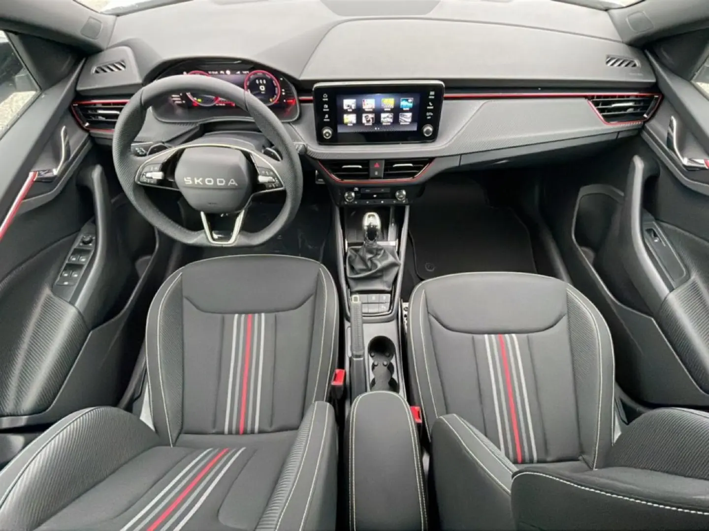 Vue intérieure frontale du Skoda Kamiq Monte Carlo 2026, sièges noirs à bandes rouges et tableau de bord avec écran tactile.