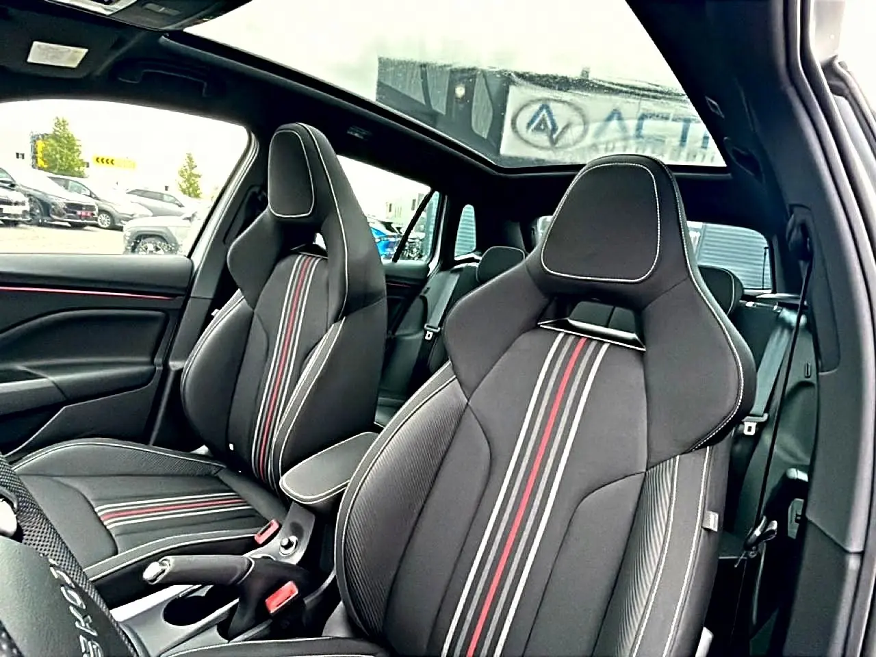 Vue intérieure côté conducteur du Skoda Kamiq blanc nacré 2026, sièges sport noirs avec bandes rouges et toit panoramique.