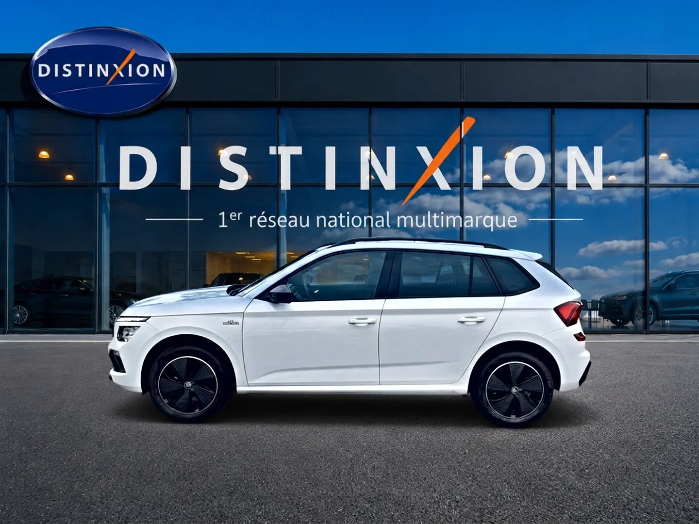 Profil droit d’un Skoda Kamiq blanc nacré 2026 avec jantes noires et toit panoramique devant une vitrine Distinxion.