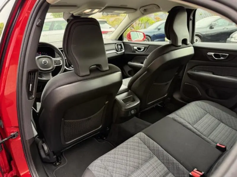 Vue intérieure arrière de la Volvo S60 rouge fusion métallisé 2024, montrant les sièges avant en cuir noir et banquette arrière grise.