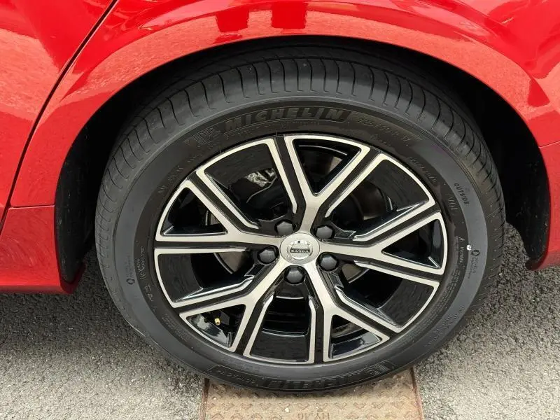 Gros plan sur la roue avant droite d'une Volvo S60 2024 Rouge Fusion Métallisé avec jante alliage noir et argent.