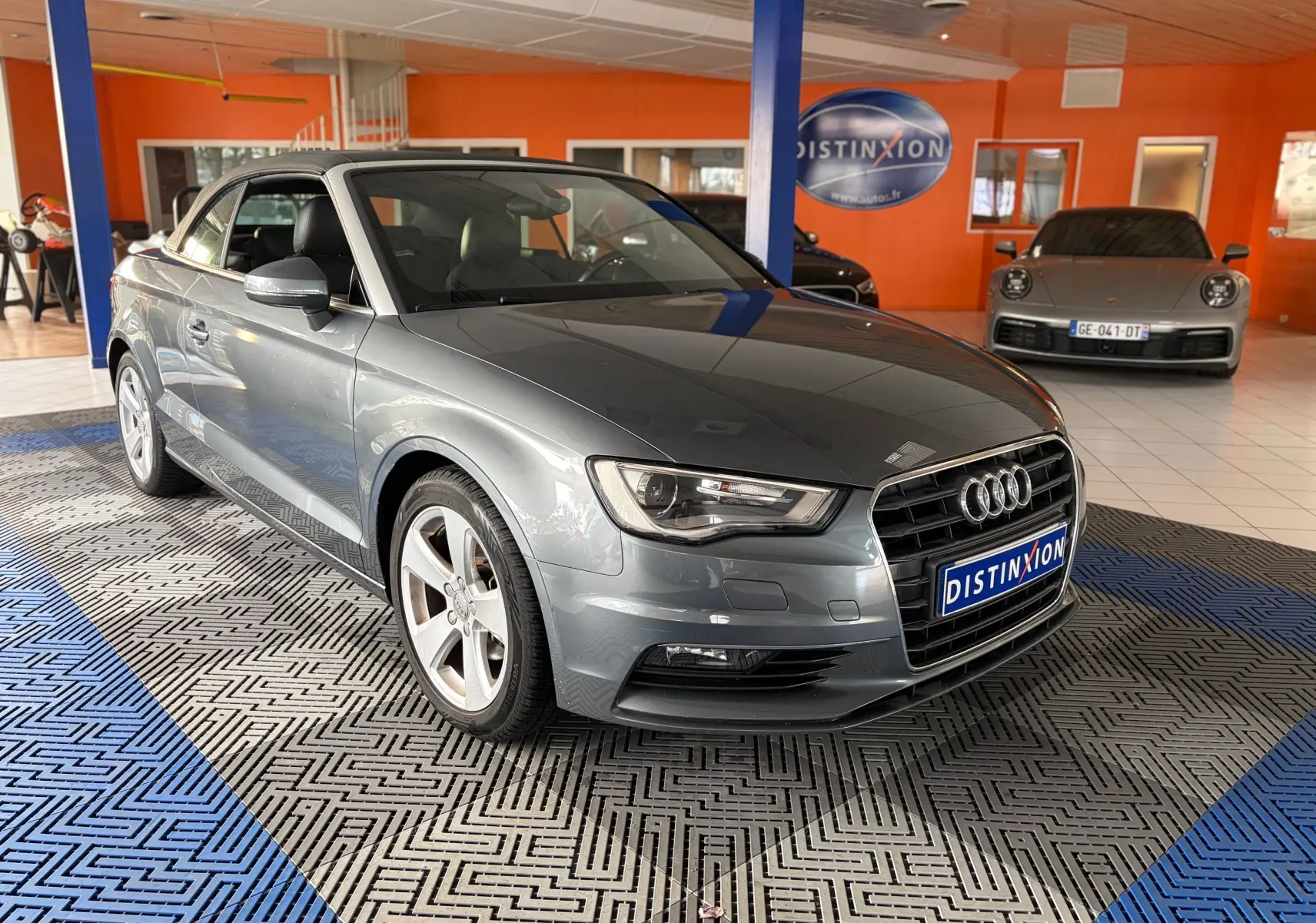 Audi A3 Cabriolet gris vue 3/4 avant droit avec capote noire dans un garage lumineux.