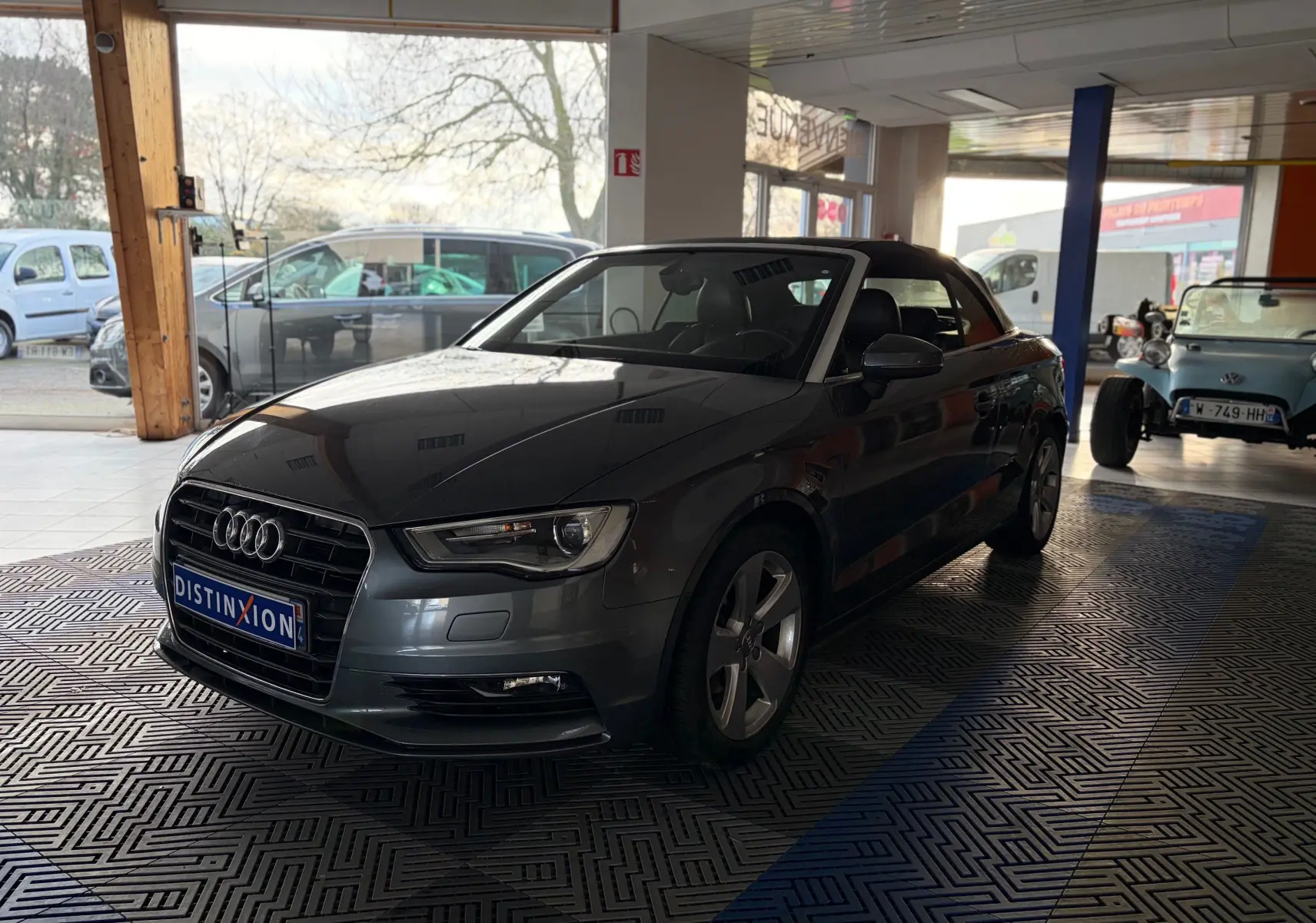 Audi A3 Cabriolet gris vue 3/4 arrière côté gauche, capote noire fermée, double sortie d'échappement visible.