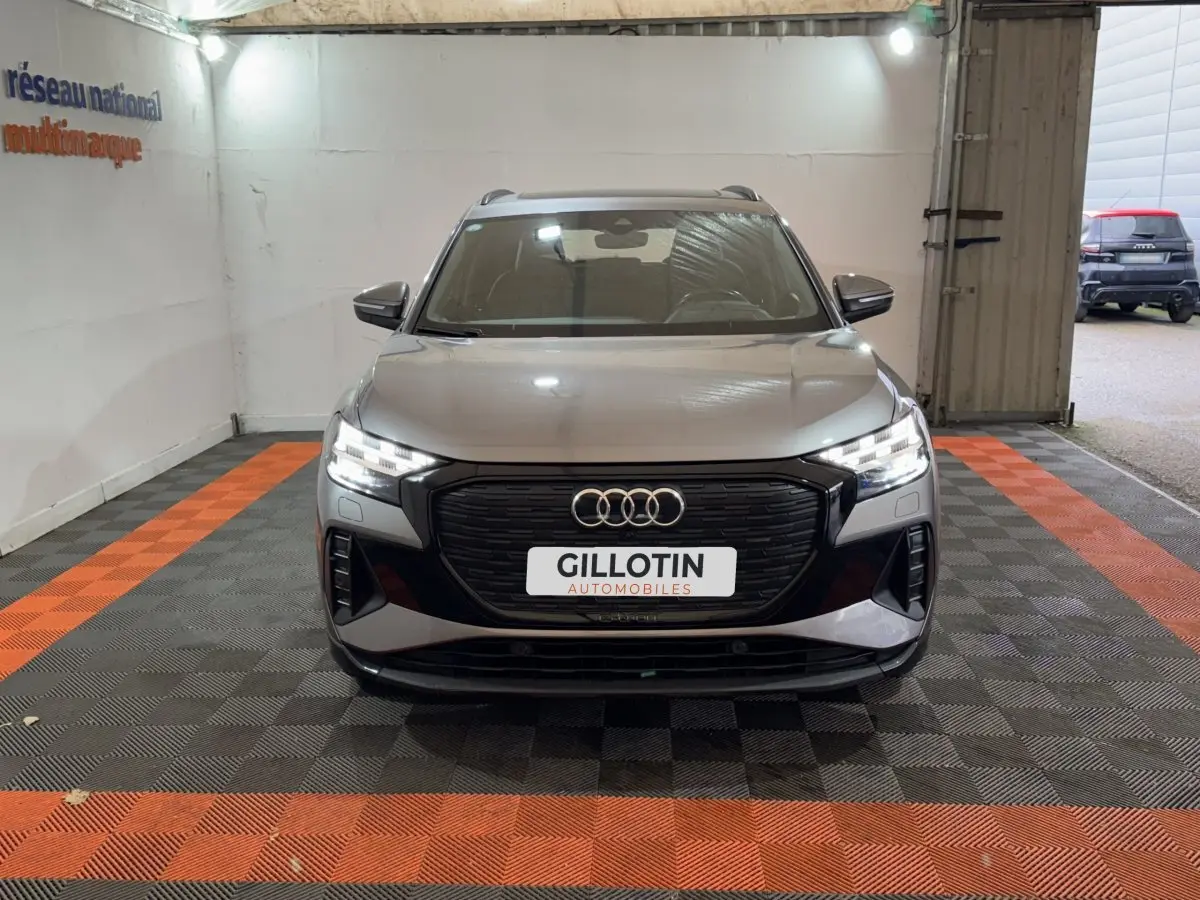 Audi Q4 E-TRON gris foncé vu de face dans un garage avec calandre noire et phares LED allumés.