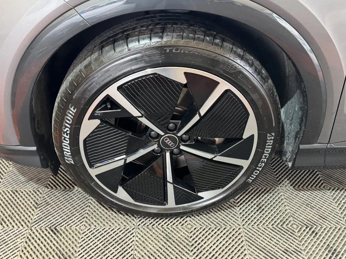 Gros plan sur la roue avant droite d'un Audi Q4 E-TRON gris foncé avec jante noire et argentée au design moderne.