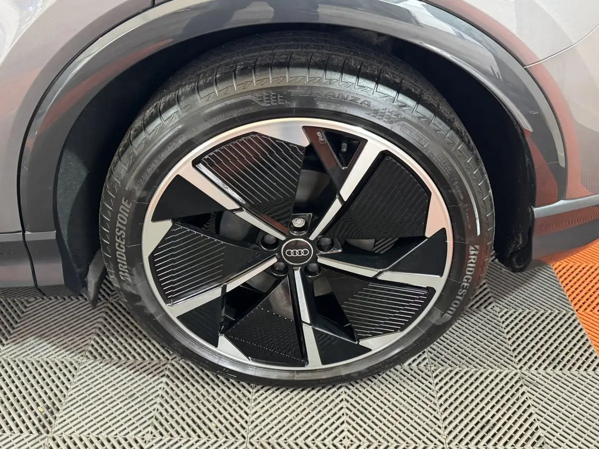 Gros plan sur la roue avant droite de l'Audi Q4 E-TRON gris foncé, jante design noir et argent avec logo Audi central.