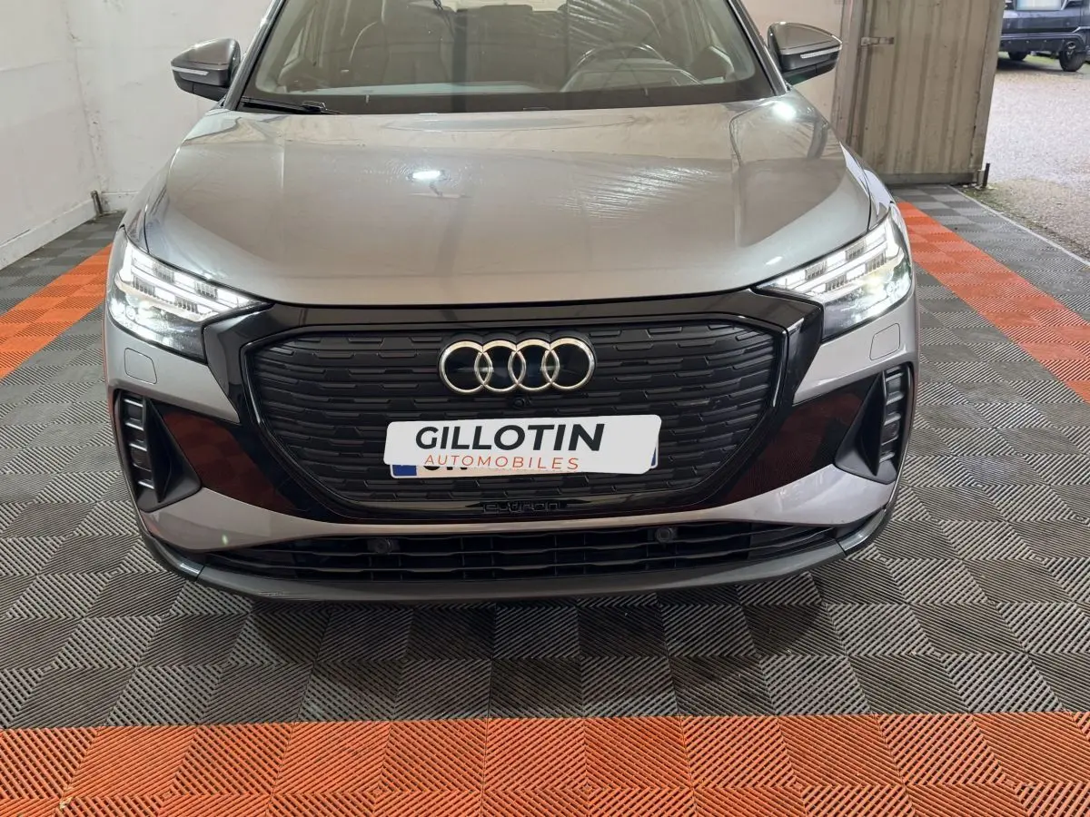 Vue avant d'un Audi Q4 E-TRON gris foncé avec calandre noire et phares LED allumés en intérieur.