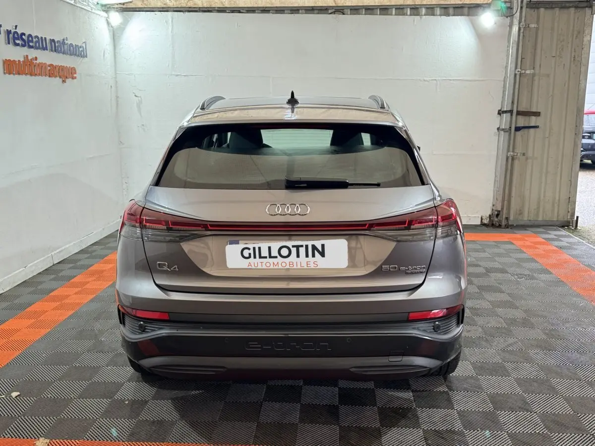 Vue arrière d'un Audi Q4 E-TRON gris foncé avec feux LED reliés et logo e-tron visible sur le pare-chocs.
