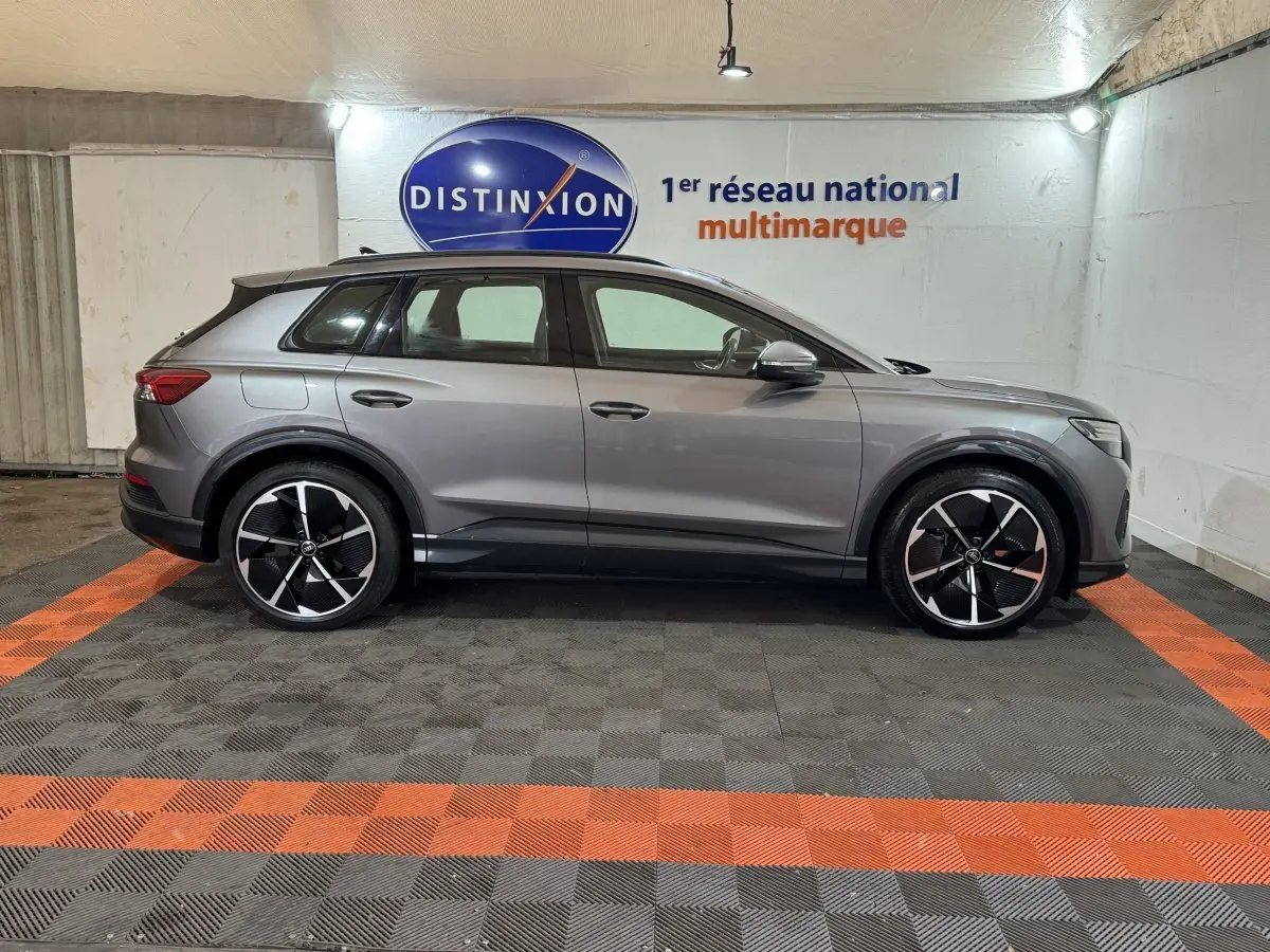 Profil droit d'un Audi Q4 E-TRON gris foncé avec jantes noires et détails chromés, stationné en intérieur.