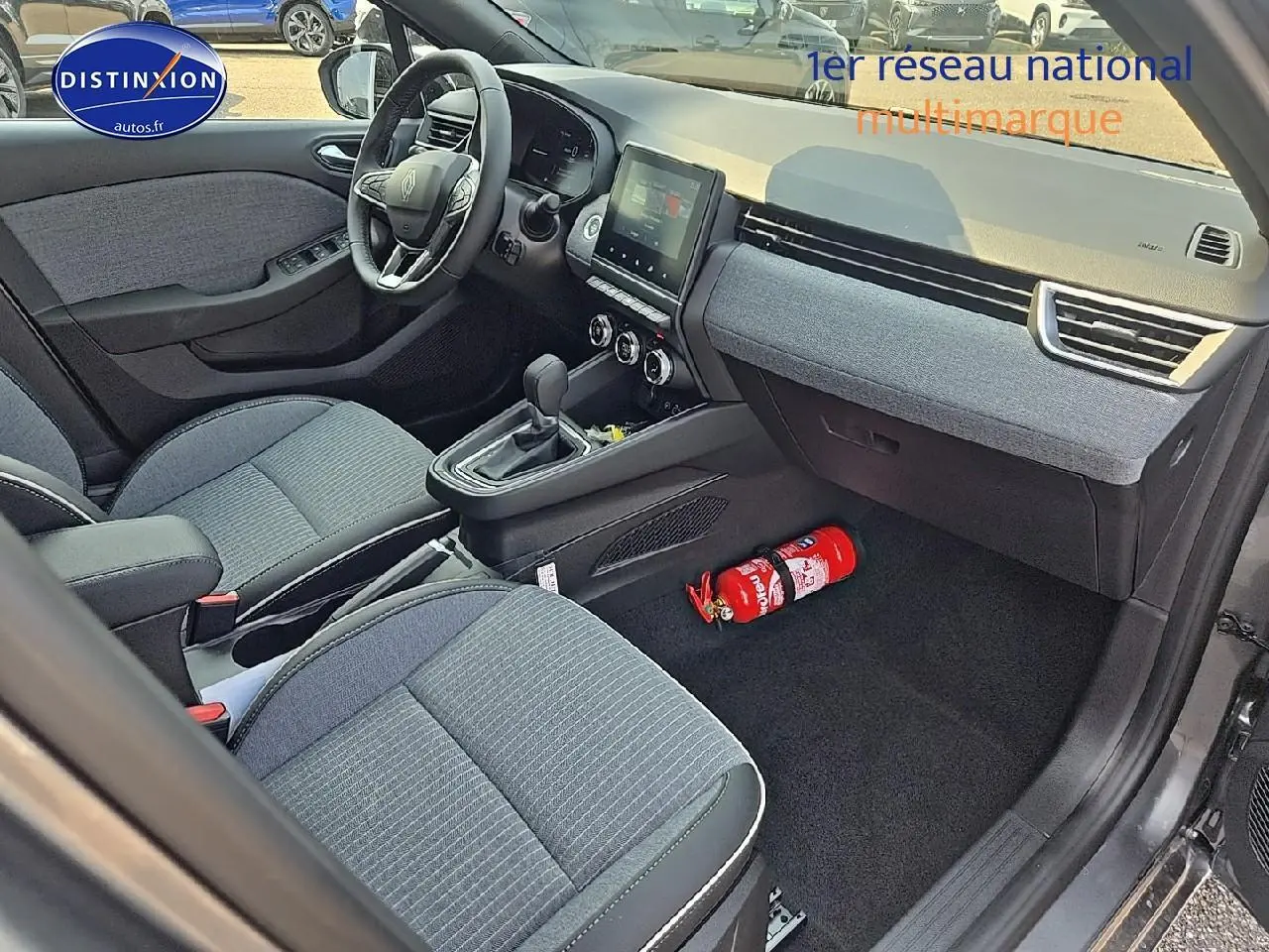 Vue intérieure avant droite de la Renault Clio V gris schiste, montrant sièges sport, console centrale et écran tactile.