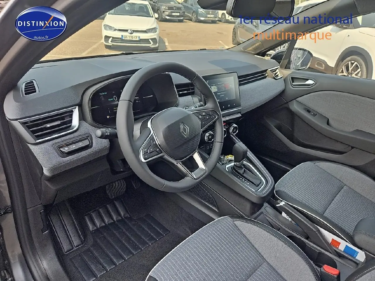 Vue intérieure avant droite de la Renault Clio V 1.6 e-tech 145 techno avec sellerie grise et tableau de bord moderne.