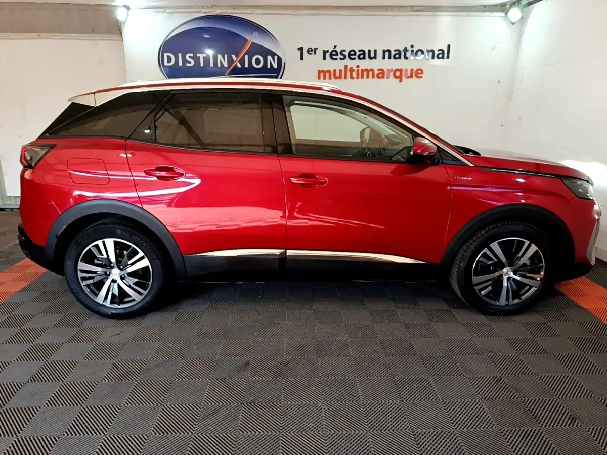 Profil droit d’un Peugeot 3008 hybride rechargeable rouge, avec jantes alliage et toit noir en intérieur showroom.