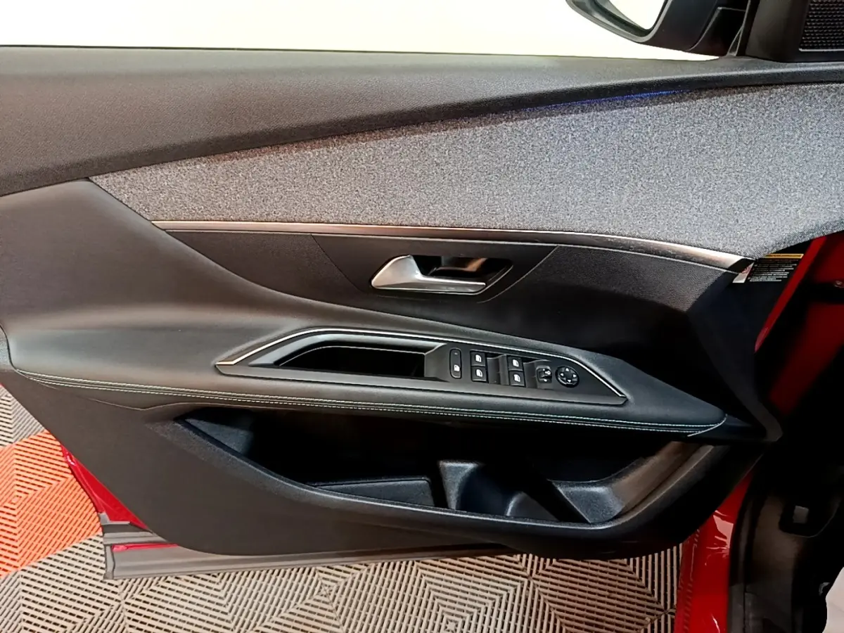 Vue intérieure côté gauche de la porte avant rouge du Peugeot 3008 avec commandes de vitres et poignée argentée.