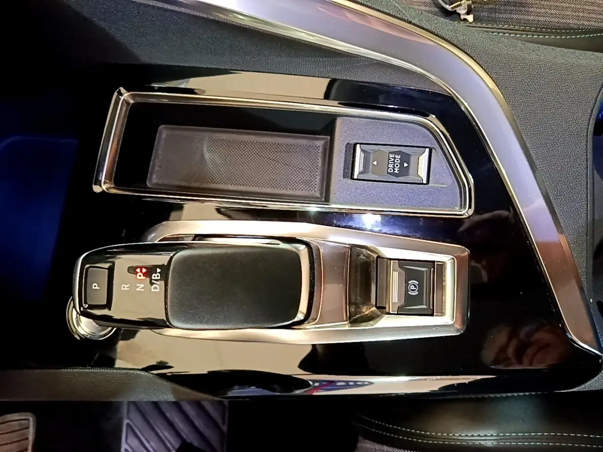 Vue rapprochée de la console centrale noire brillante du Peugeot 3008 hybride, avec levier de vitesses automatique et bouton Drive Mode.