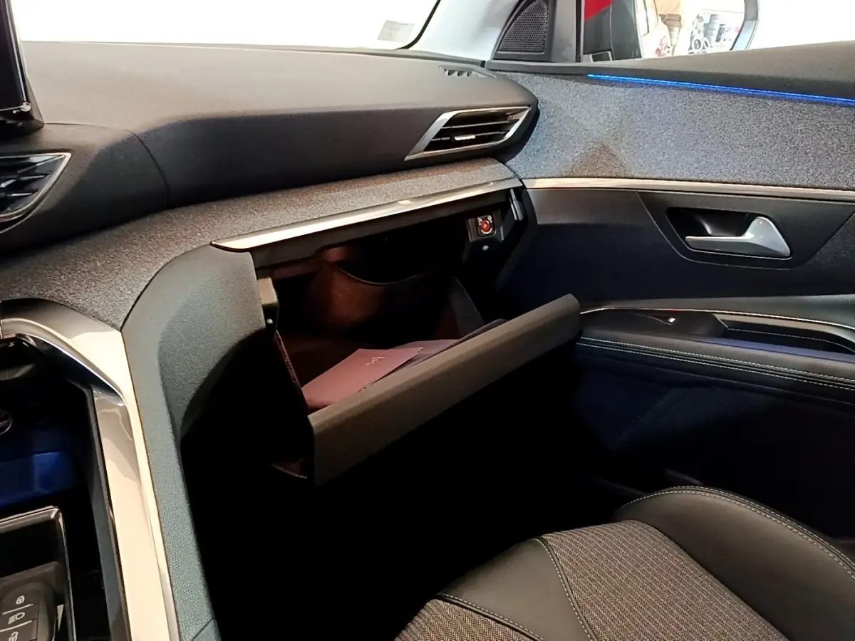 Vue intérieure côté passager du Peugeot 3008 hybride 2021 avec boîte à gants ouverte et éclairage d’ambiance bleu.