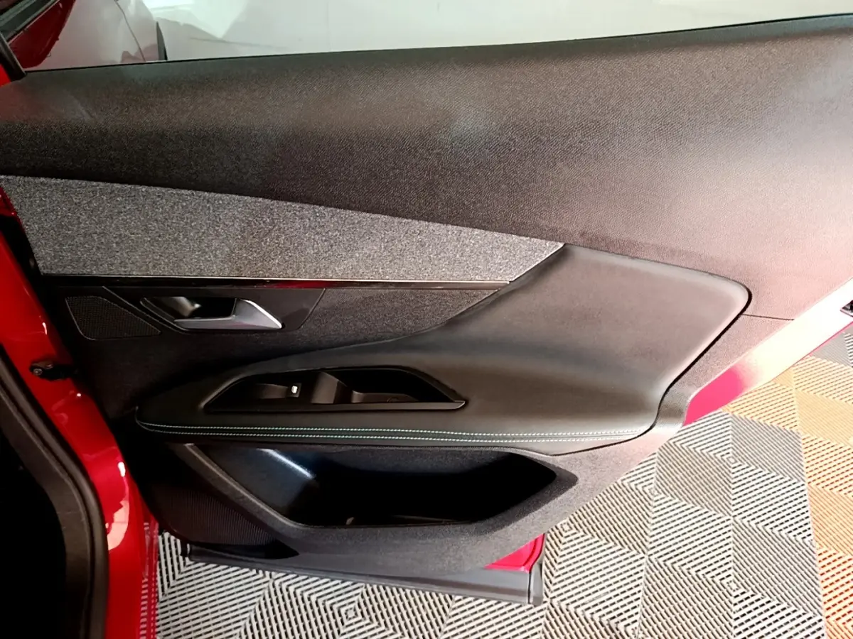 Vue intérieure côté gauche de la porte avant rouge du Peugeot 3008 1.6 HYBRID avec garniture noire et tissu gris.