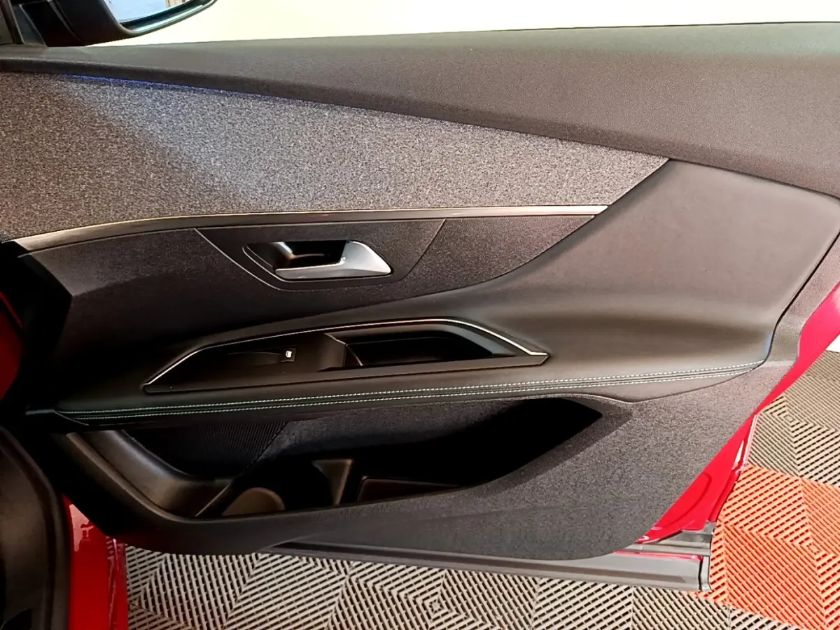 Vue intérieure côté gauche de la porte avant rouge du Peugeot 3008 avec garniture noire et insert tissu gris.