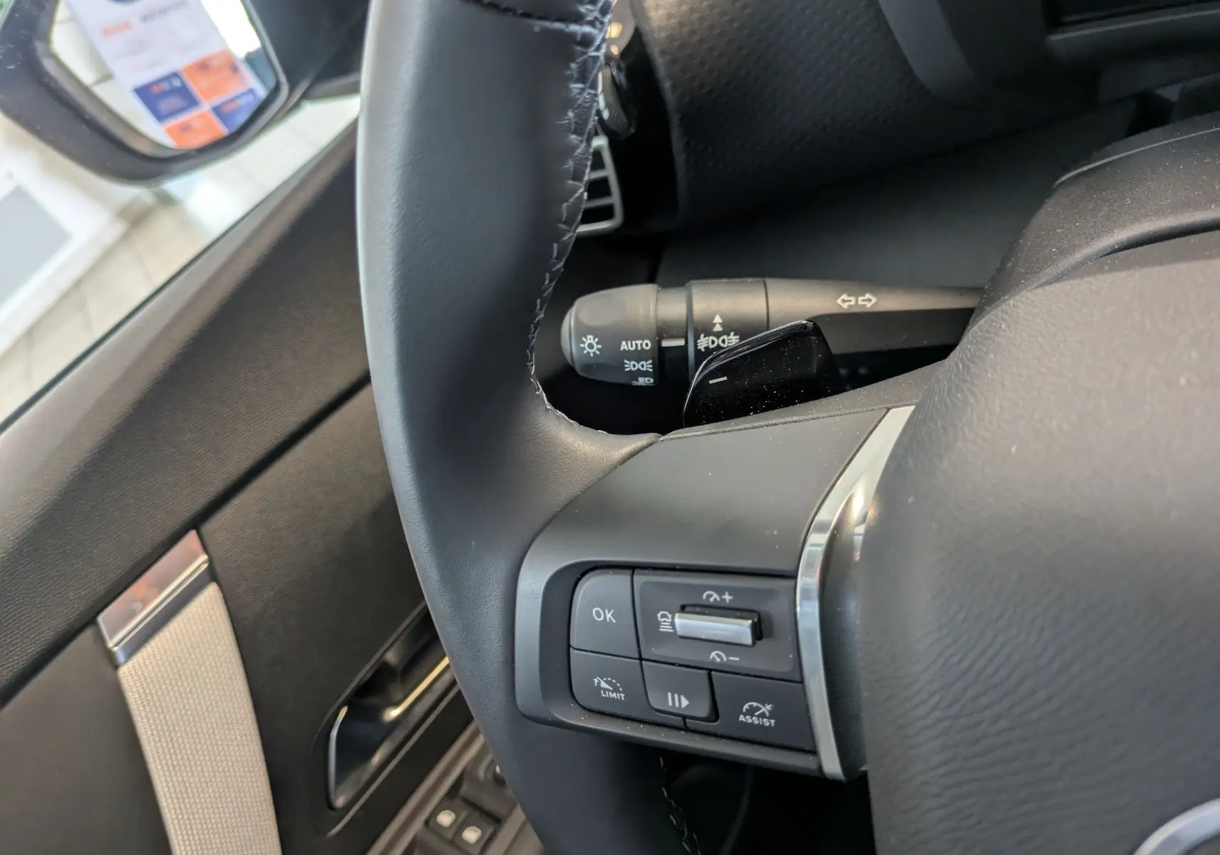 Gros plan sur le volant noir côté gauche de la Citroën C4 1.2 Hybride 2025 avec commandes intégrées et partie de la portière visible.