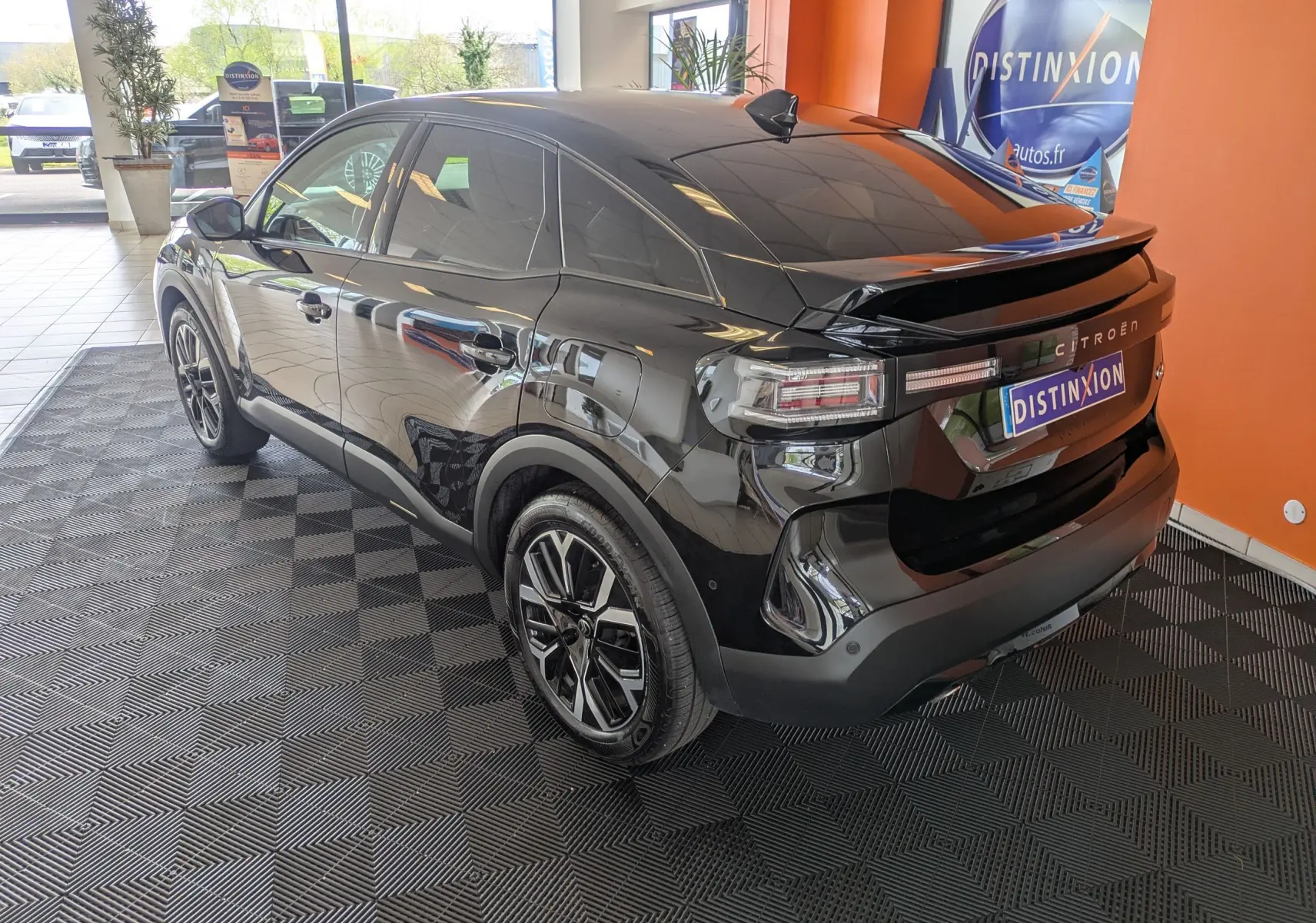 Vue 3/4 arrière droite d'une Citroën C4 noire 2025 en hybride, avec jantes biton et toit incliné dans un showroom.