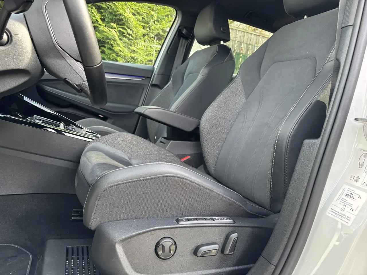 Vue intérieure côté conducteur de la Volkswagen Golf blanche 2024, mettant en valeur le siège avant en tissu et cuir avec réglages électriques.