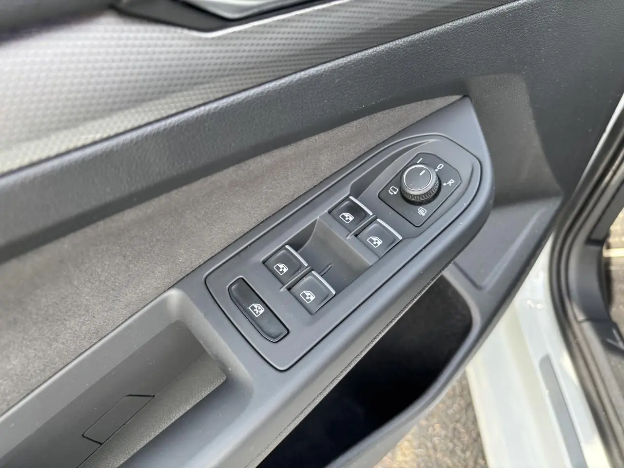 Vue rapprochée des commandes des vitres et des rétroviseurs sur la porte côté gauche d'une Volkswagen Golf blanche 2024.