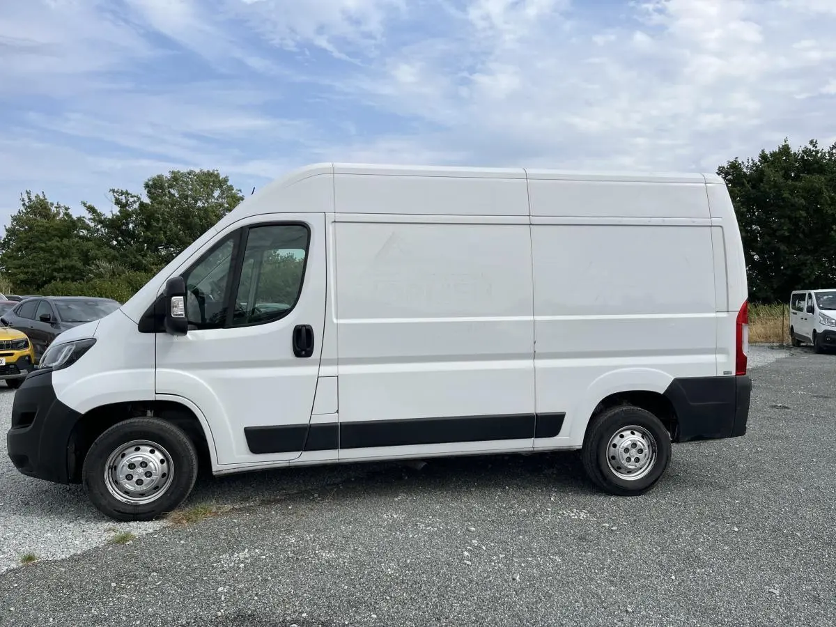 Vue de profil côté gauche d’un Peugeot Boxer Fourgon blanc avec porte latérale coulissante tôlée sur un parking extérieur.