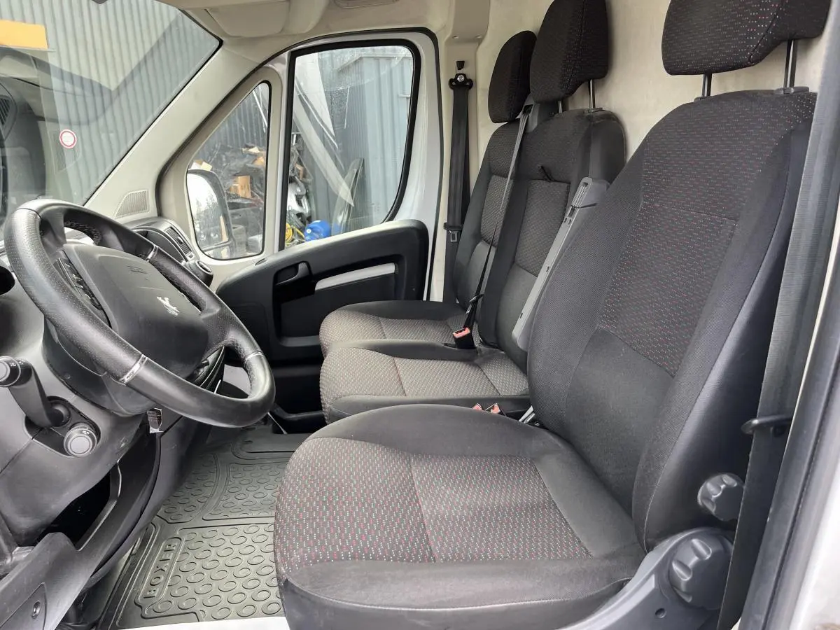 Vue intérieure côté conducteur du Peugeot Boxer Fourgon 2023, sièges tissu noir avec motifs rouges et volant cuir.