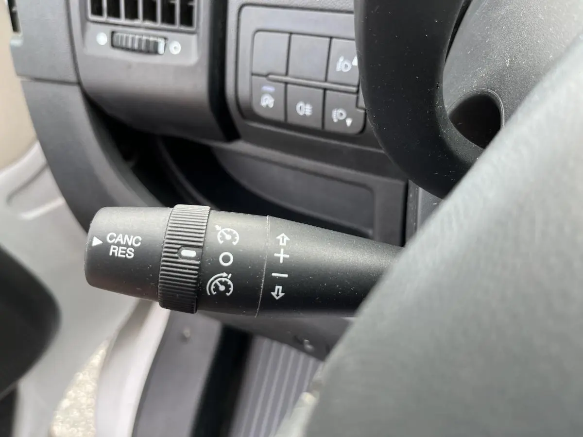 Gros plan sur la commande de régulateur de vitesse à gauche du volant dans l'habitacle du Peugeot Boxer blanc.